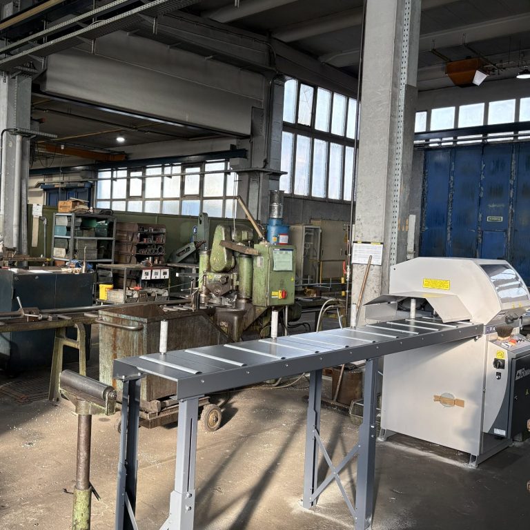 Fertigungshalle mit Maschinen und Rollenbahnen in industrieller Umgebung.