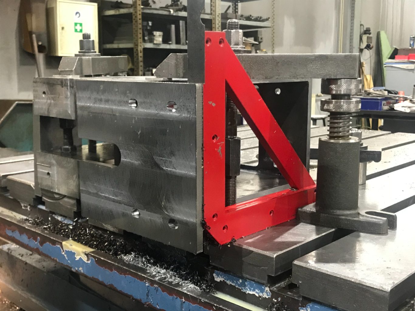 Schweißkonstruktion auf CNC-Fräsmaschine Metallmaschine mit rotem Haltewinkel und Werkstückspannung auf einem Fertigungsarbeitsplatz.