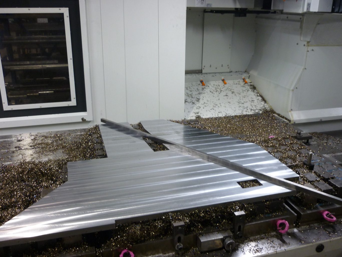 Fräsbearbeitung bis 1600mm x 2000mm Metallplatte auf einer Bearbeitungsmaschine mit Spänen im Hintergrund.