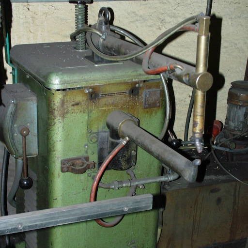 Alte, grüne Maschinen mit Rohren und Schläuchen in einer Werkstatt.